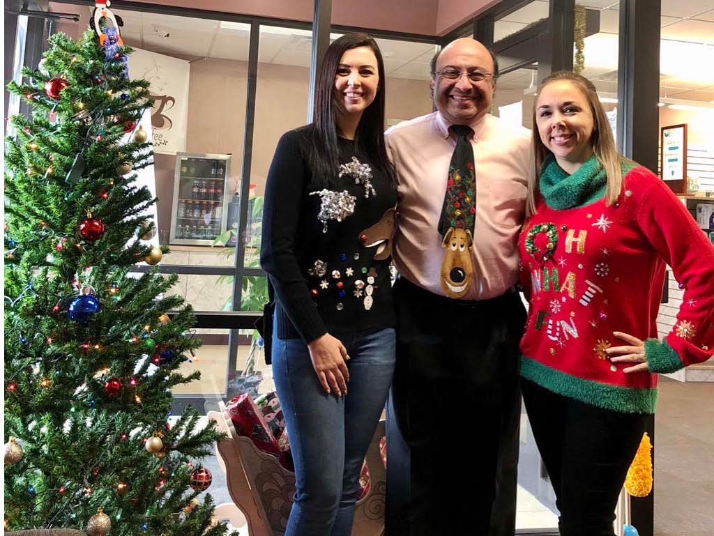 Three people standing beside a decorated Christmas tree indoors, smiling at the camera.