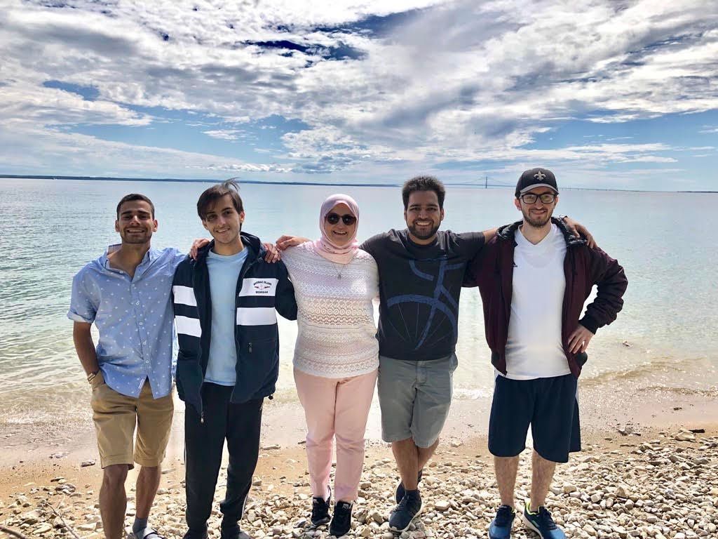 Five friends posing on a beach with the sea and cloudy sky behind them
