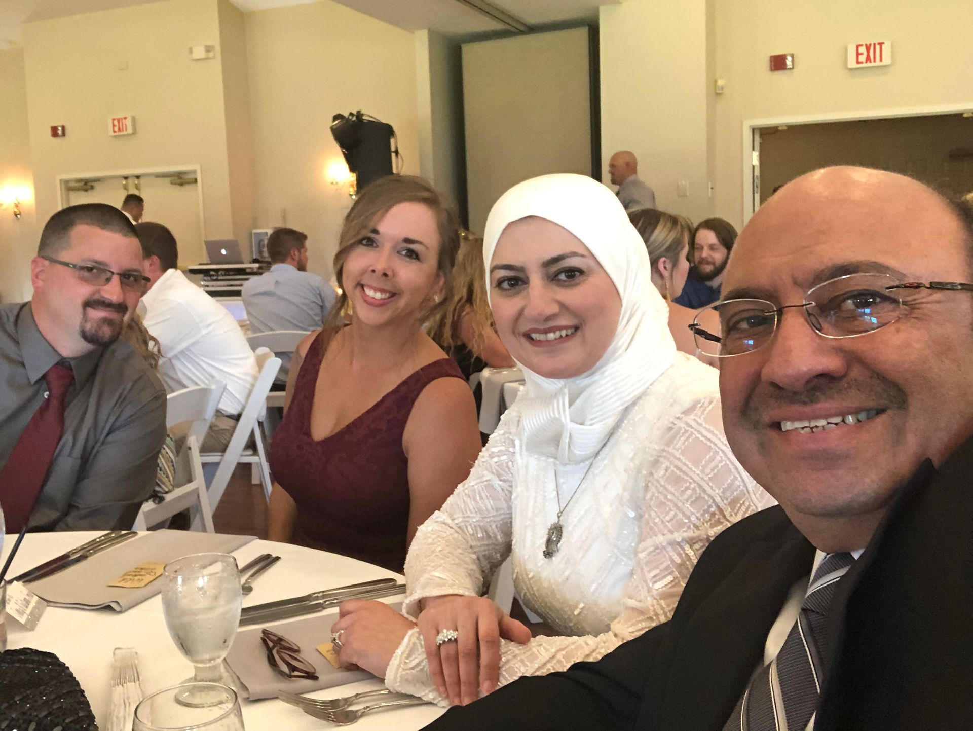 Four smiling people seated at a banquet table in a bright event hall, with drinks and place settings.