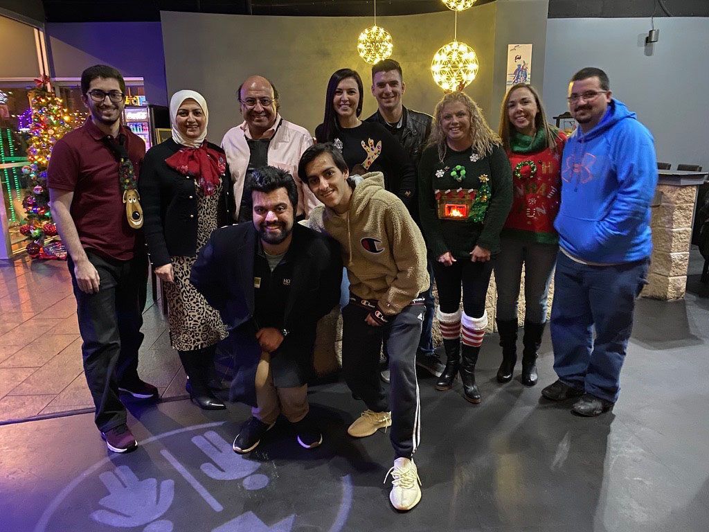 Group of people posing together indoors with holiday lights and decorations in the background.