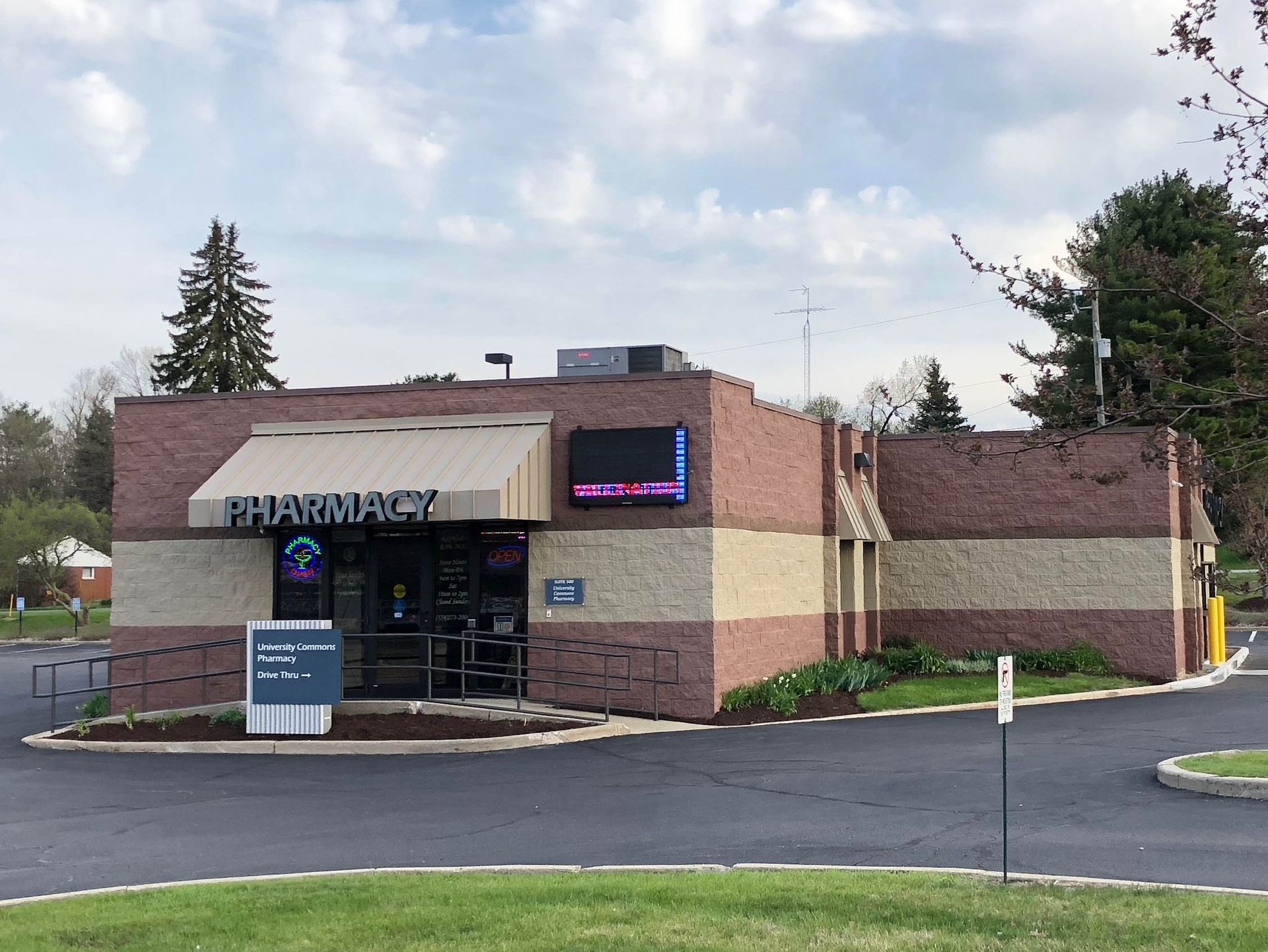 Pharmacy storefront in a brick building with a dark parking lot and cloudy sky