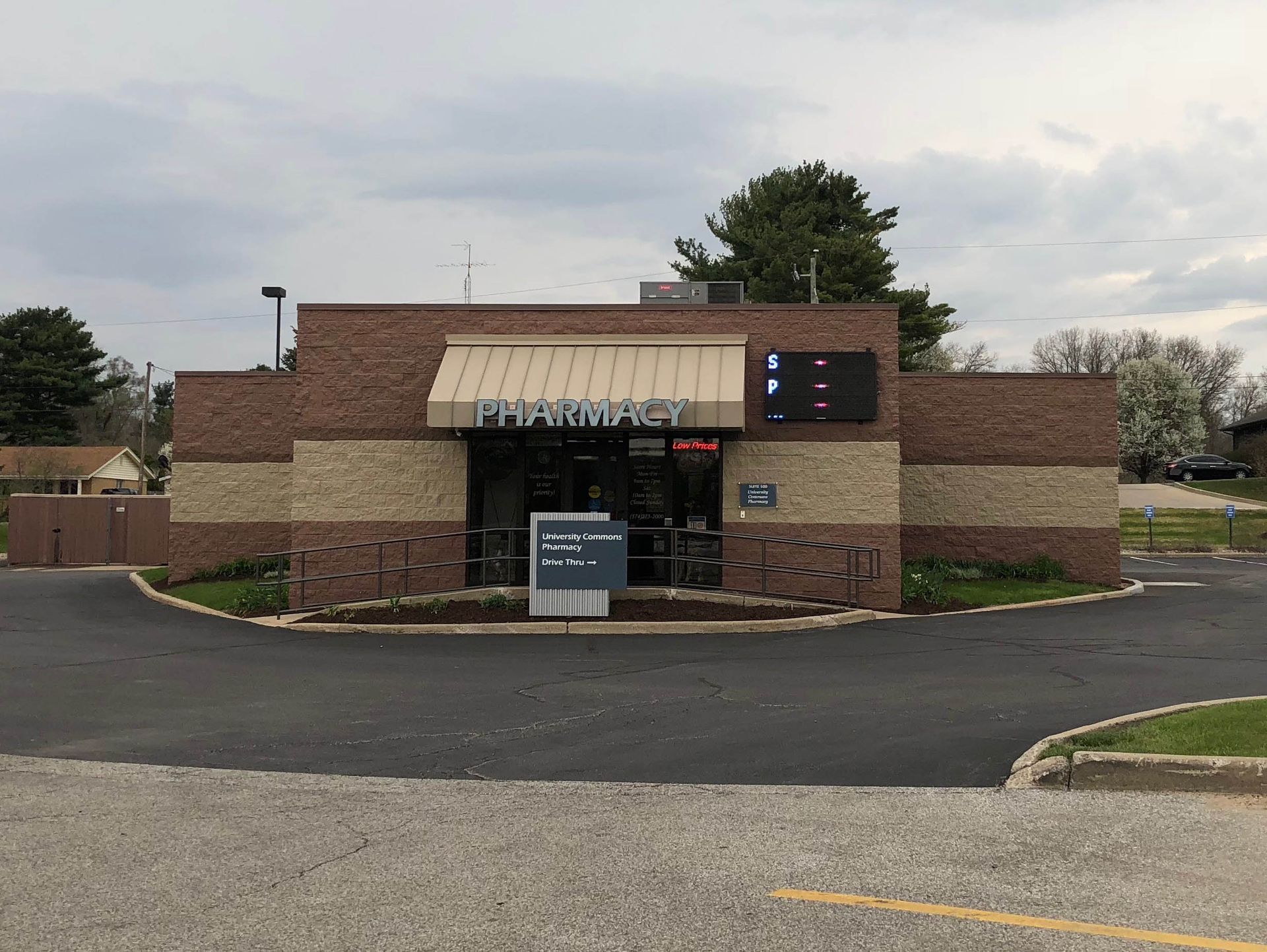 Brick storefront with a striped awning and drive-thru lane under a cloudy sky.