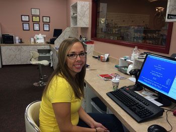 Woman seated at a desk in an office, smiling at a computer with a blue screen.