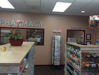Pharmacy interior with shelves of products, a counter, and a large “PHARMACY” sign on the wall