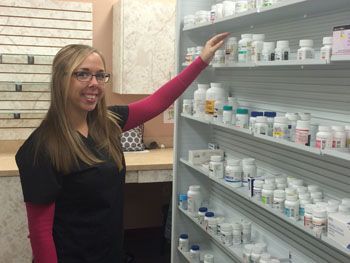 Woman in black and pink points to shelves of labeled bottles in a pharmacy or clinic storage room