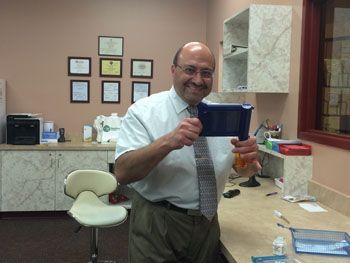 Man in a tie smiling and holding a blue cup in a beige office/lab room