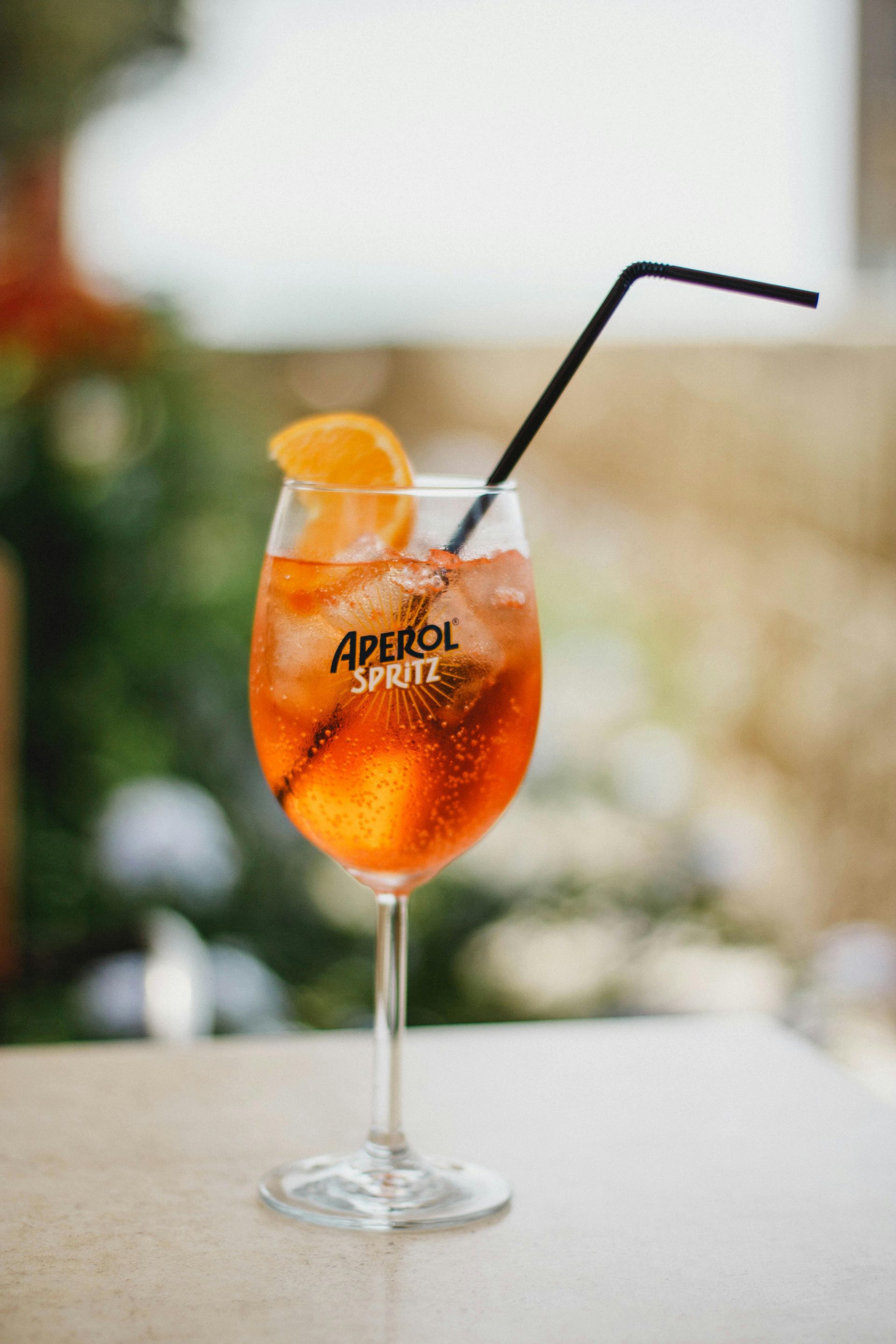 A glass of aperol spritz with a straw on a table.