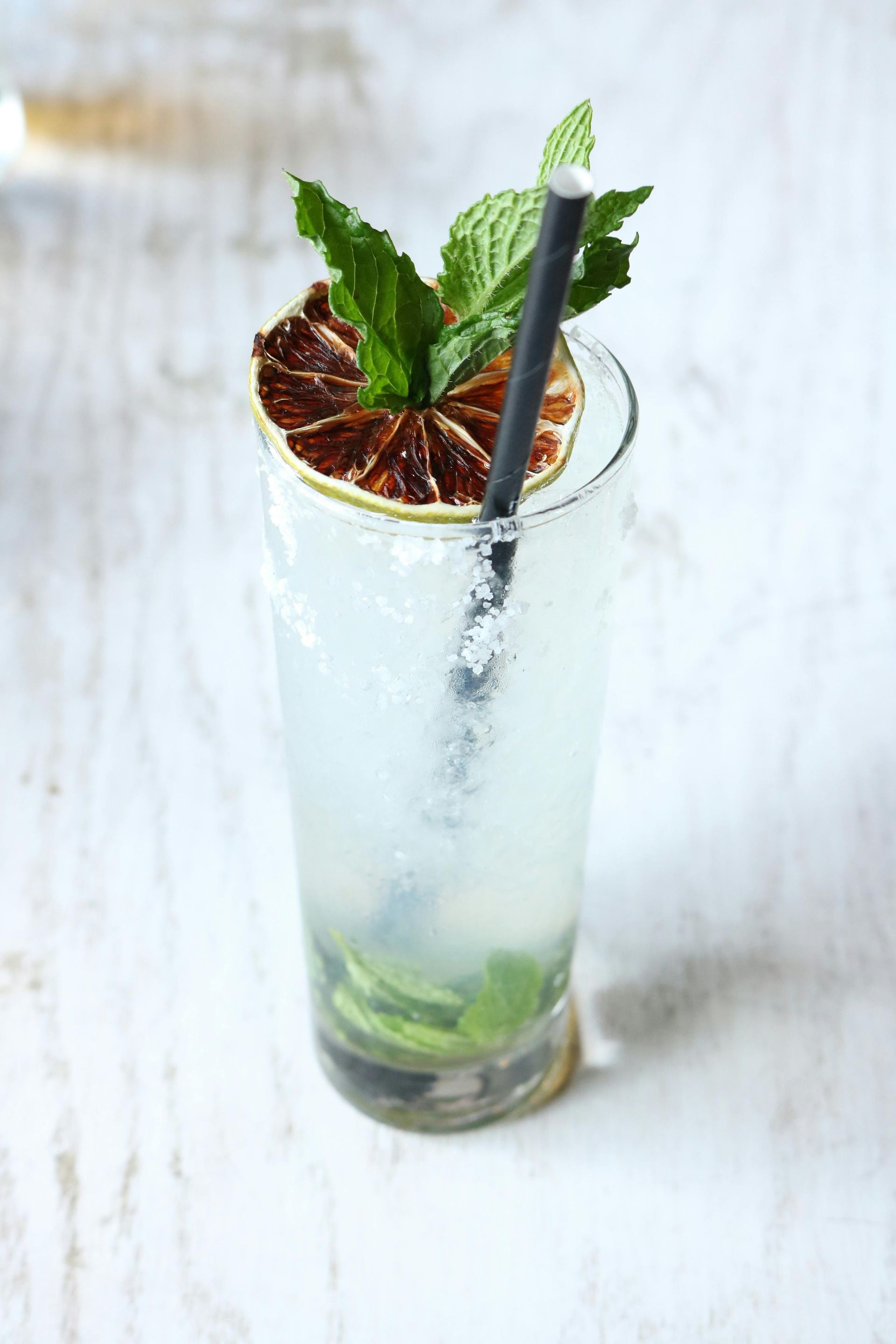 A drink in a tall glass with a straw and mint leaves on top.
