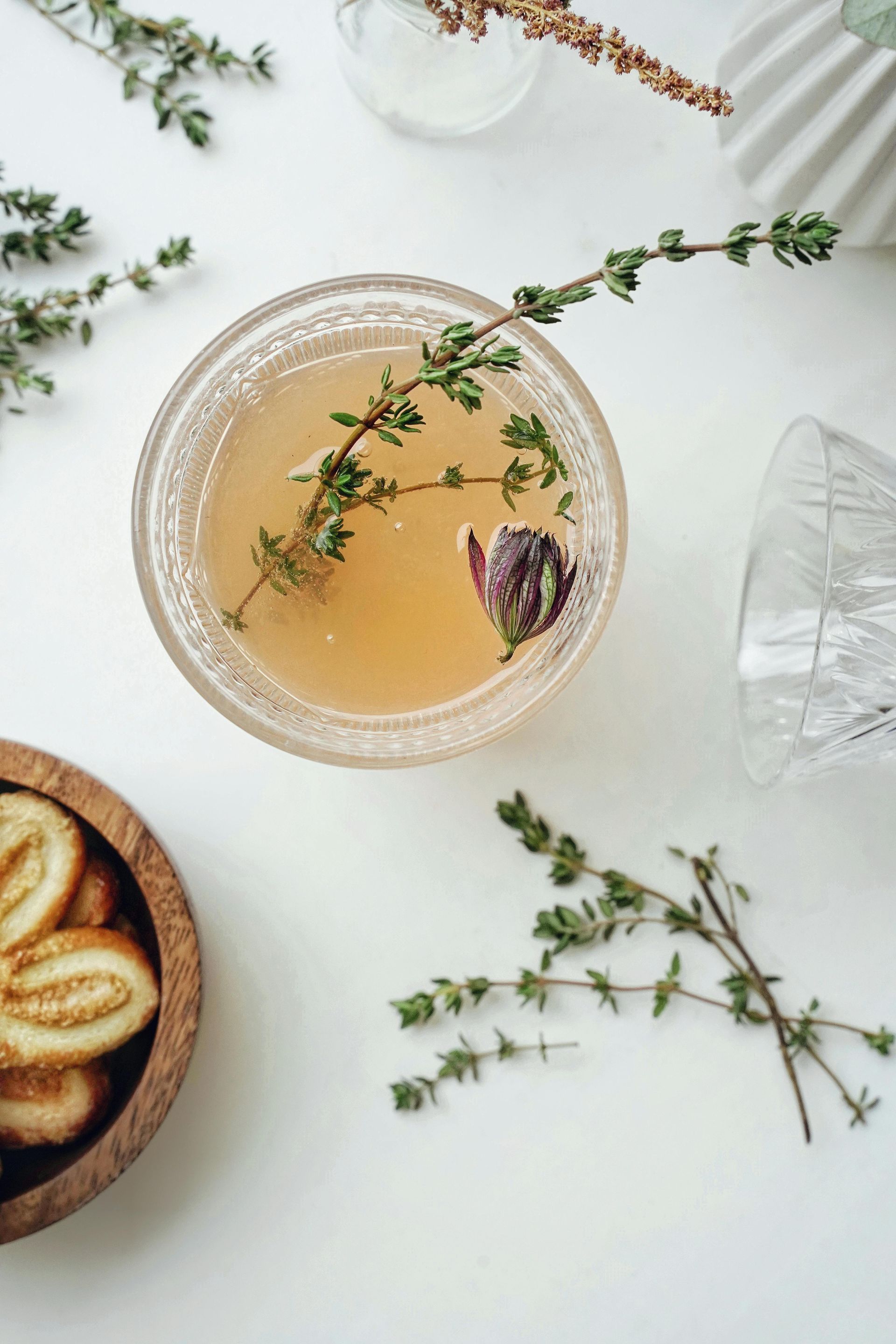 A glass of tea with thyme and lemon slices on a table.