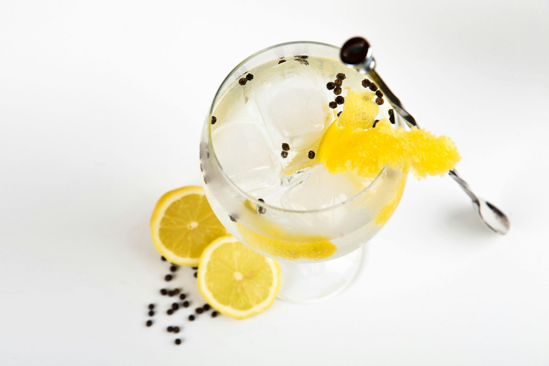 A glass of gin and tonic with lemon slices and a spoon.