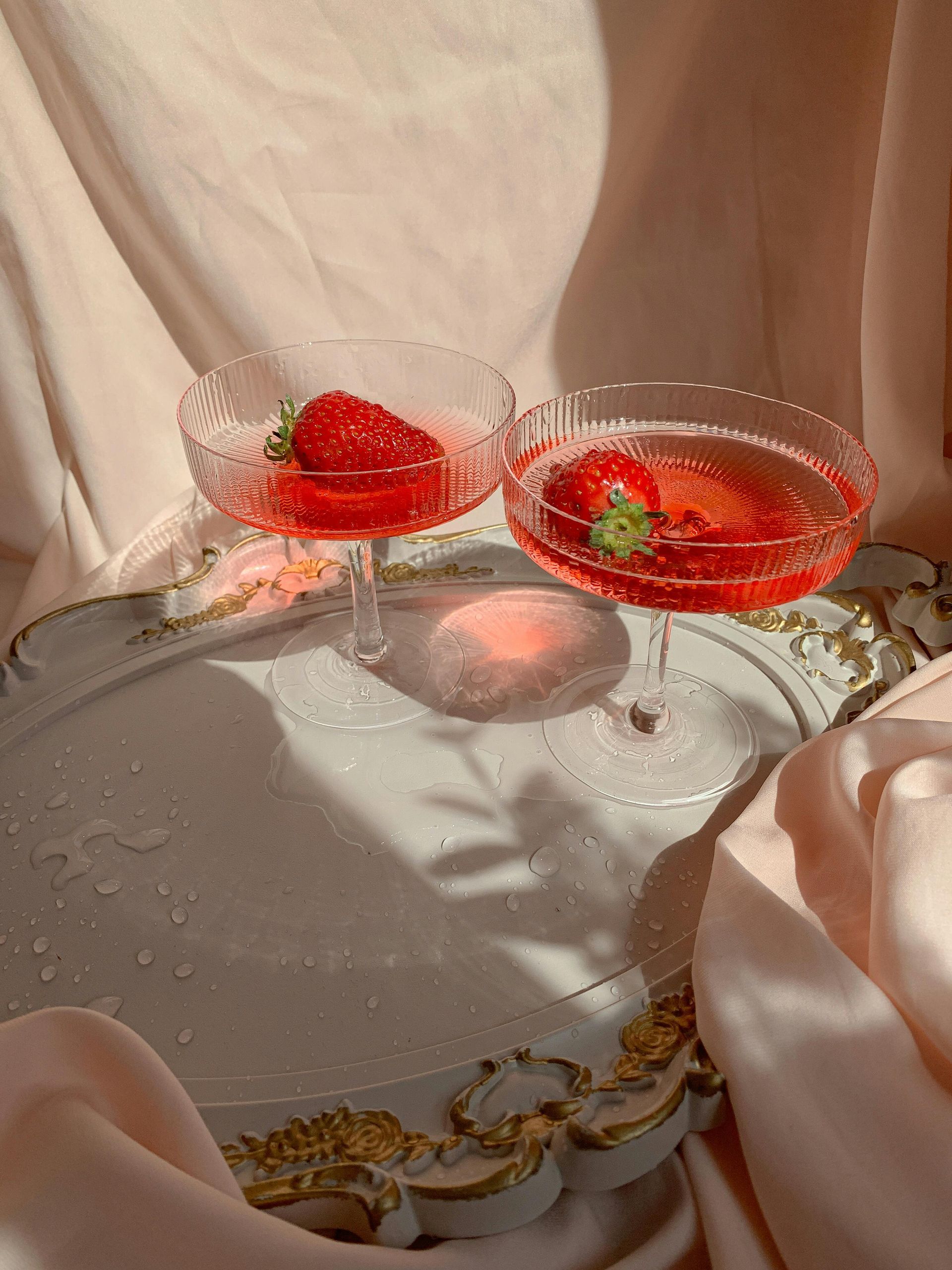 Two champagne glasses filled with red liquid and strawberries on a plate.