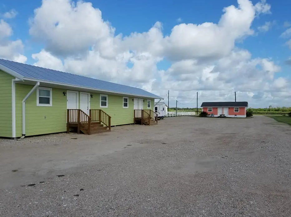 A row of green houses are sitting next to each other on a gravel road.