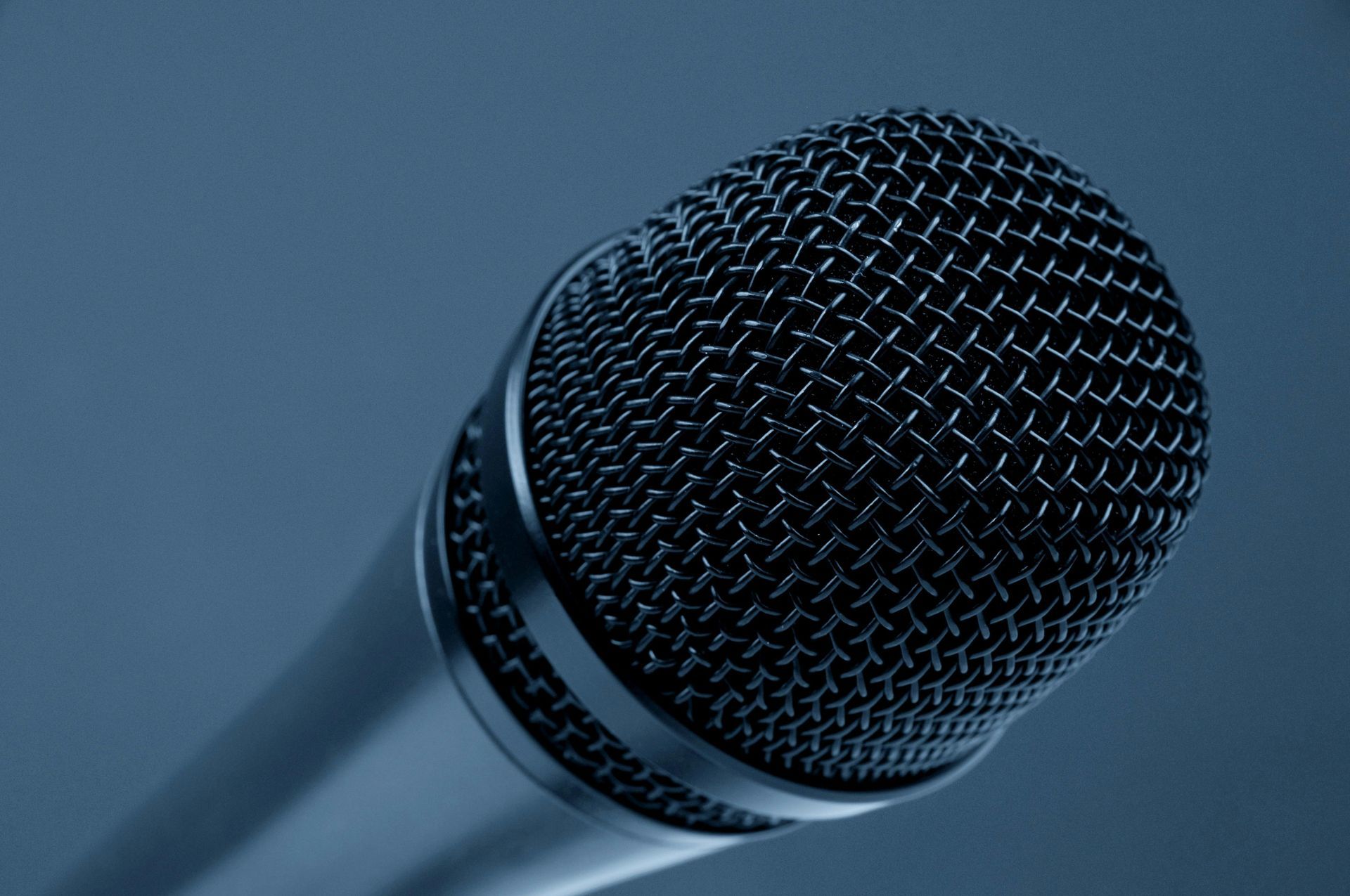 Close-up of a black microphone with a mesh head against a blue-gray background.