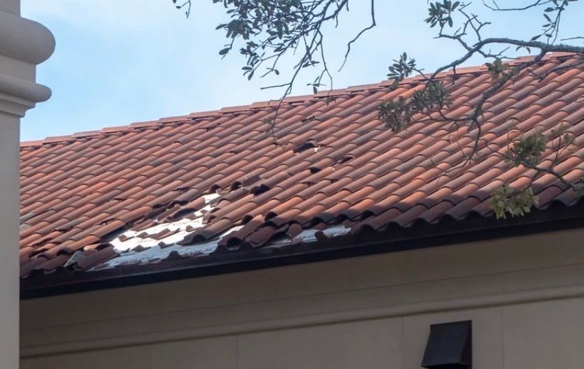 Red clay tile roof with patches of melting snow beside a beige wall and column
