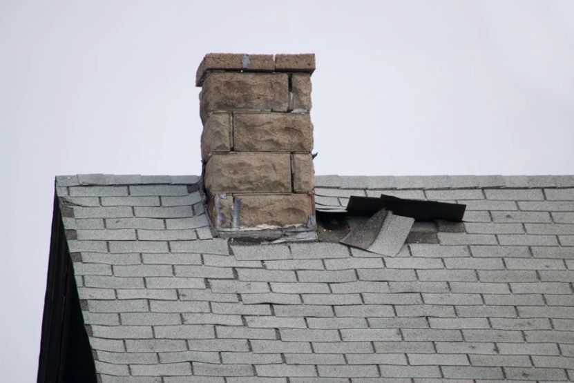Damaged shingle roof with a stone chimney and missing shingles near the base
