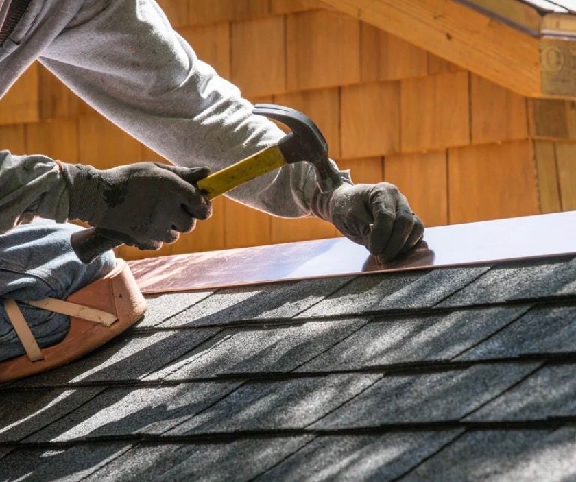 Two workers installing shingles on a roof with a hammer and gloves