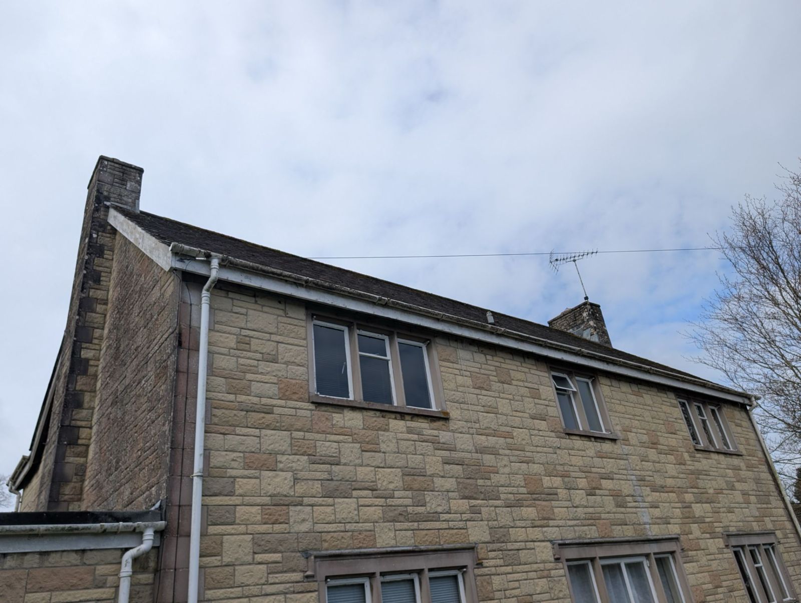 Stone house exterior under a cloudy sky, with two upper windows and a chimney.