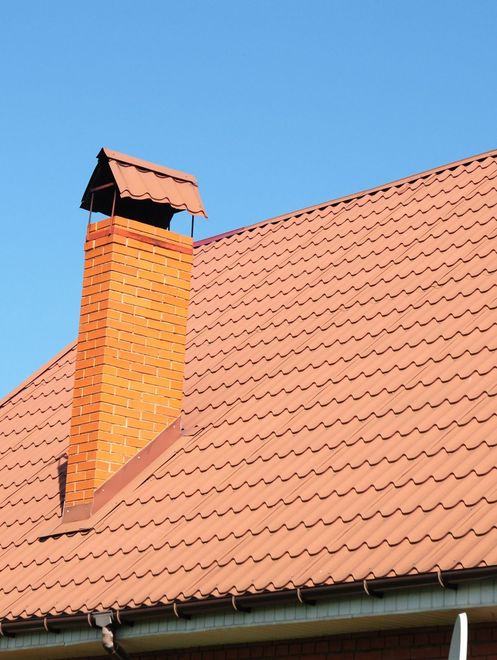 Red-tiled house roof with orange brick chimney against a blue sky