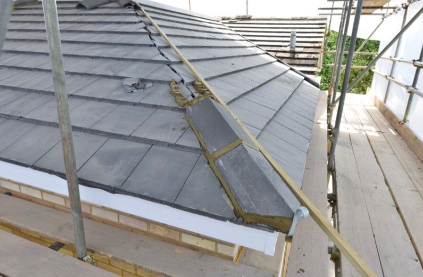 Roof under construction with a ladder on a scaffold beside gray shingles