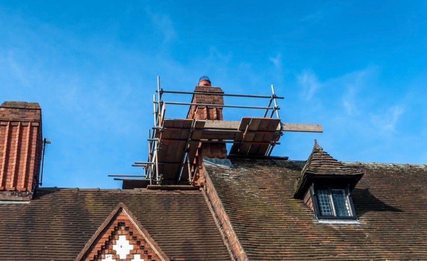 Rooftop with scaffolding and a brick chimney against a bright blue sky