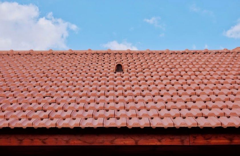 Red clay-tiled roof against a blue sky with a small vent opening near the top center