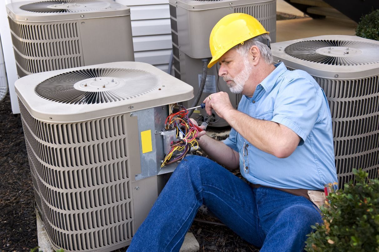 A Man is Sitting on the Ground Working on an Air Conditioner — Air-Con Cleaning Specialists in Redlynch, QLD