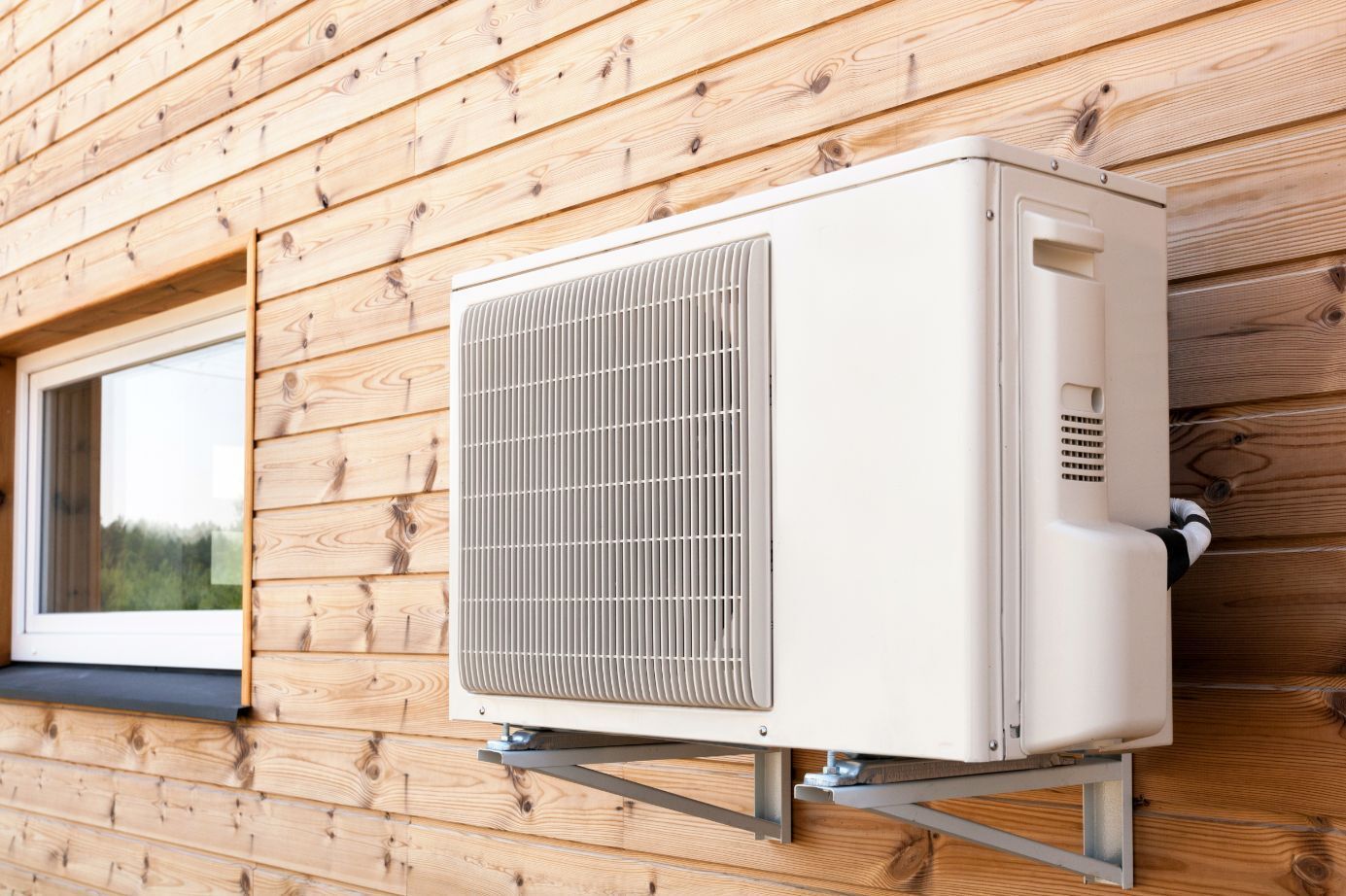 A White Air Conditioner is Mounted on a Wooden Wall Next to a Window — Air-Con Cleaning Specialists in Redlynch, QLD