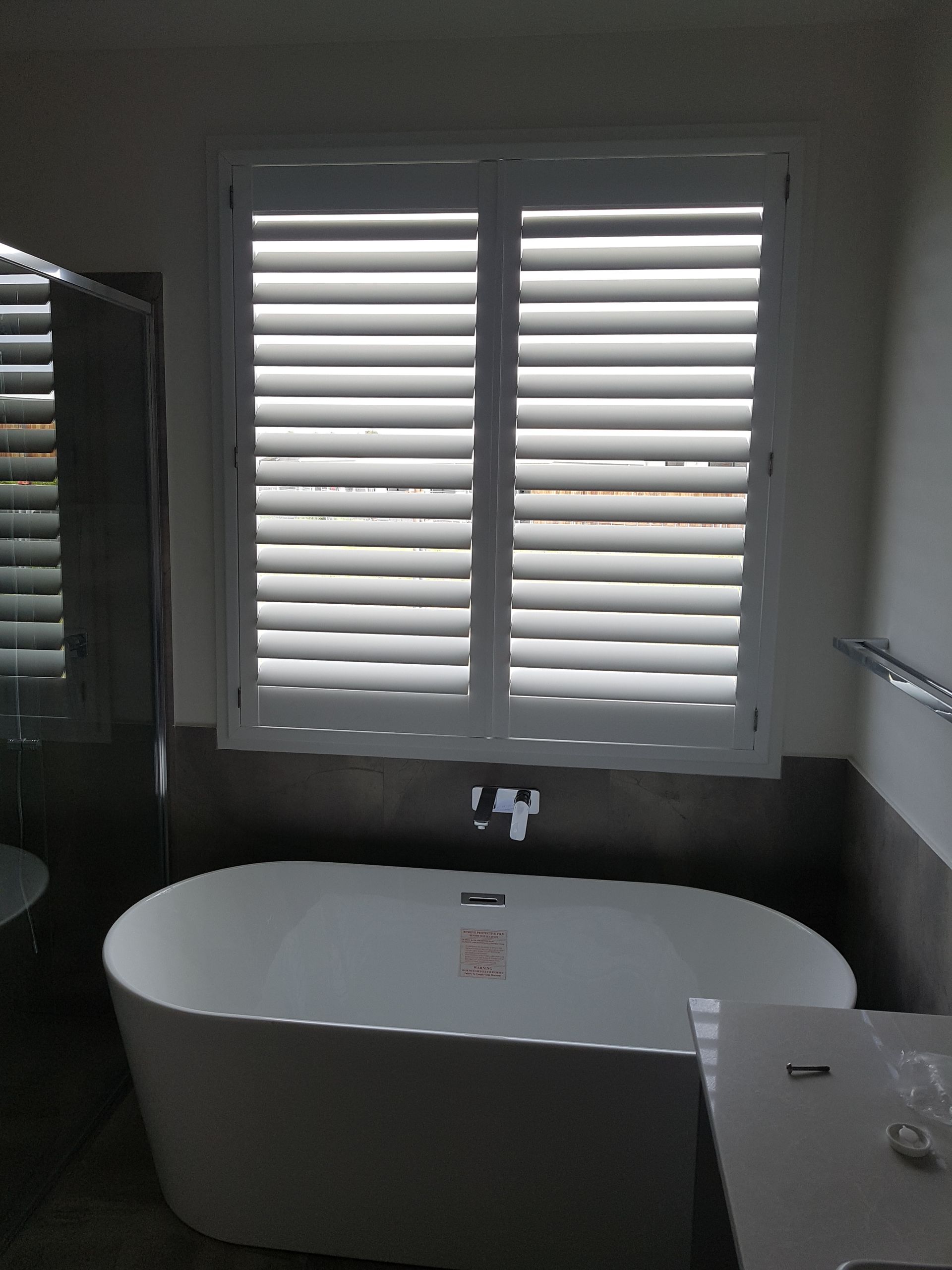 A Bathtub in a Bathroom With Shutters on the Window — Bevan Plumbing in South Lismore, NSW