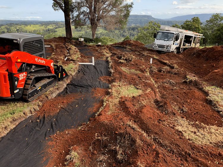 A Bulldozer is Driving Down a Dirt Road Next to a Truck — Bevan Plumbing in South Lismore, NSW