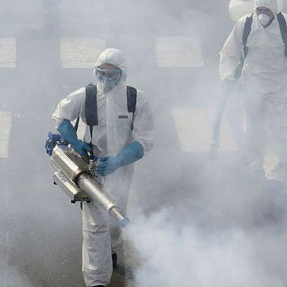 Two people in hazmat suits spraying disinfectant, creating a cloud of mist.