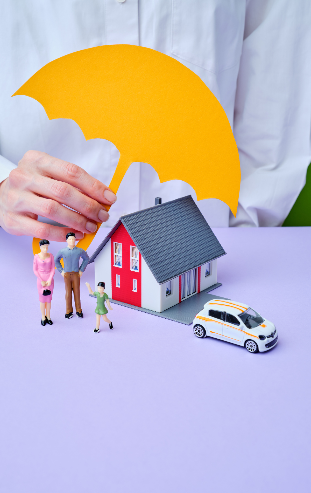 A person is holding an umbrella over a model house and car.