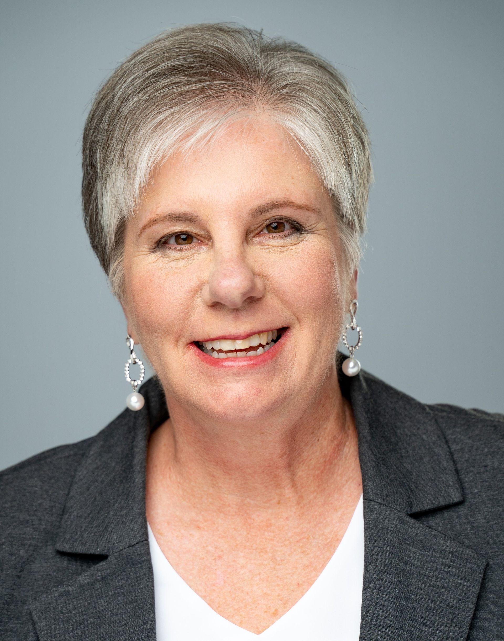 A woman wearing a gray jacket and earrings is smiling for the camera.