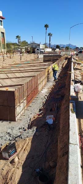 Construction site with wooden forms for concrete walls, worker in safety vest, sunny day.