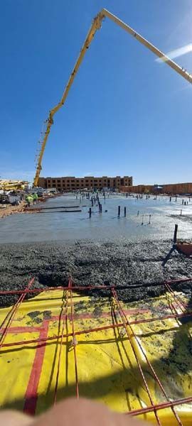 Construction site with concrete being poured, blue sky, steel rebar, yellow tarp.