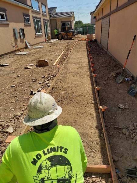 Construction worker inspecting a narrow path with wooden forms, between two buildings, preparing for concrete.