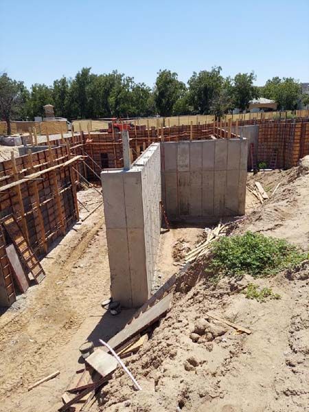 Construction site with concrete walls, wooden forms, and earth. Bright, sunny day.