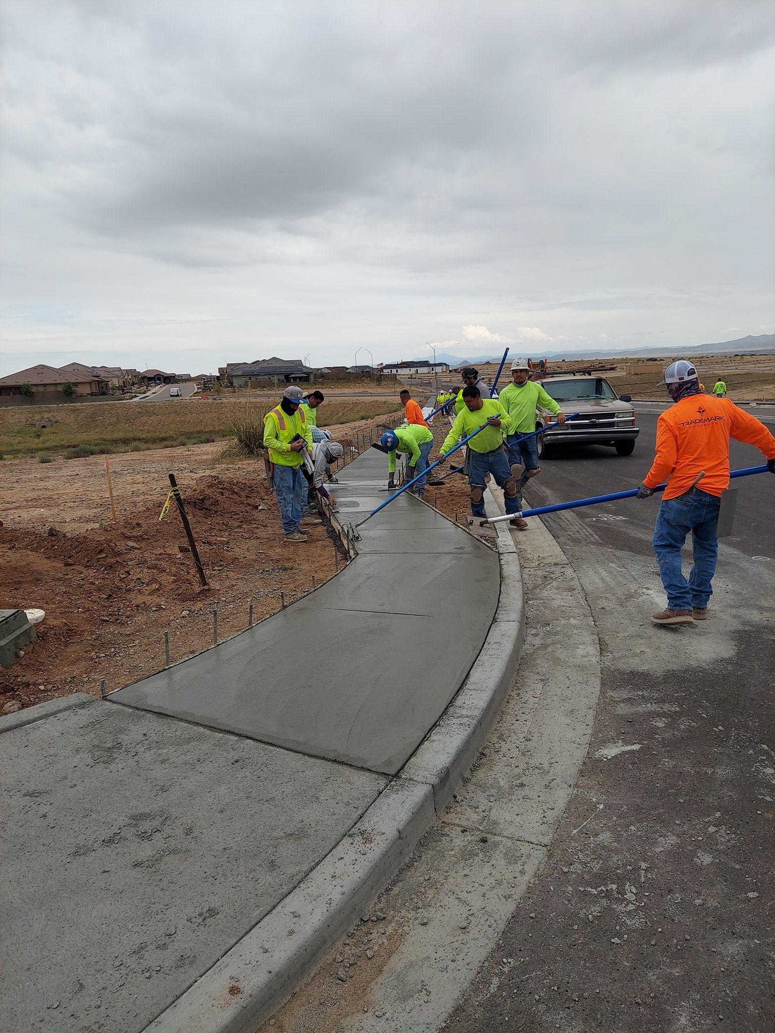 Construction workers smoothing wet concrete for a sidewalk curb on a cloudy day.
