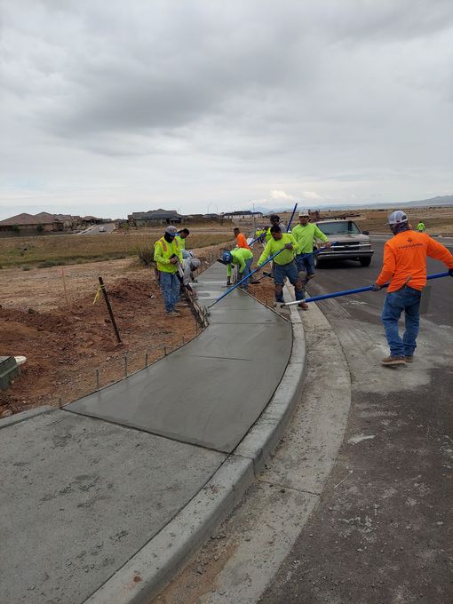 Construction workers smoothing wet concrete for a sidewalk curb on a cloudy day.