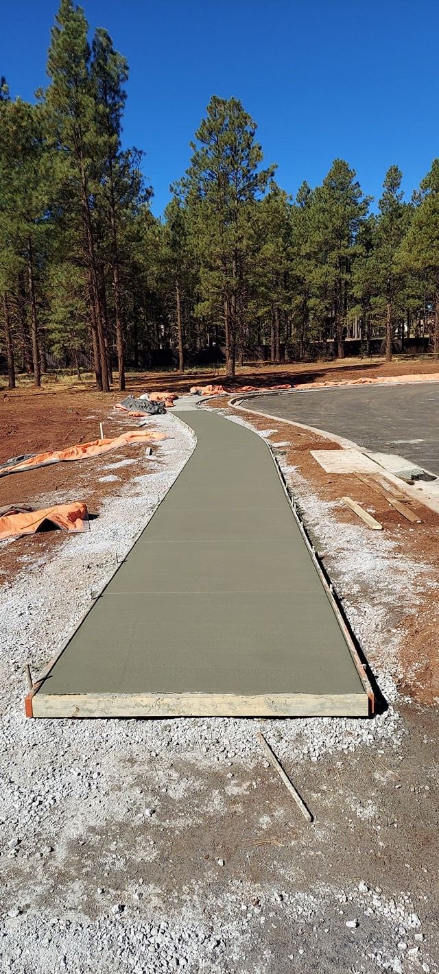 A newly poured concrete walkway winds through a natural setting under a clear blue sky.