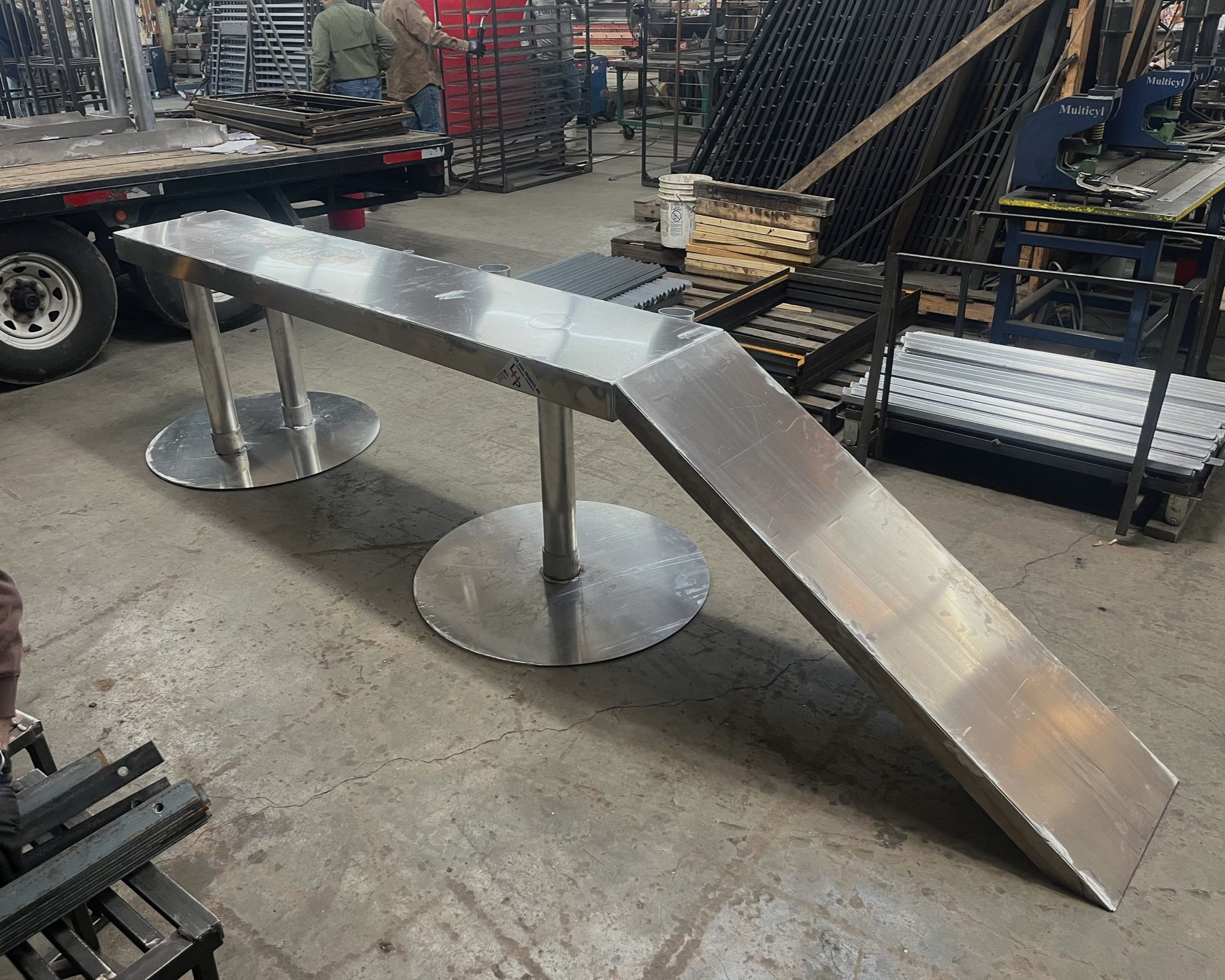 Stainless steel workbench with two round base supports in a workshop.