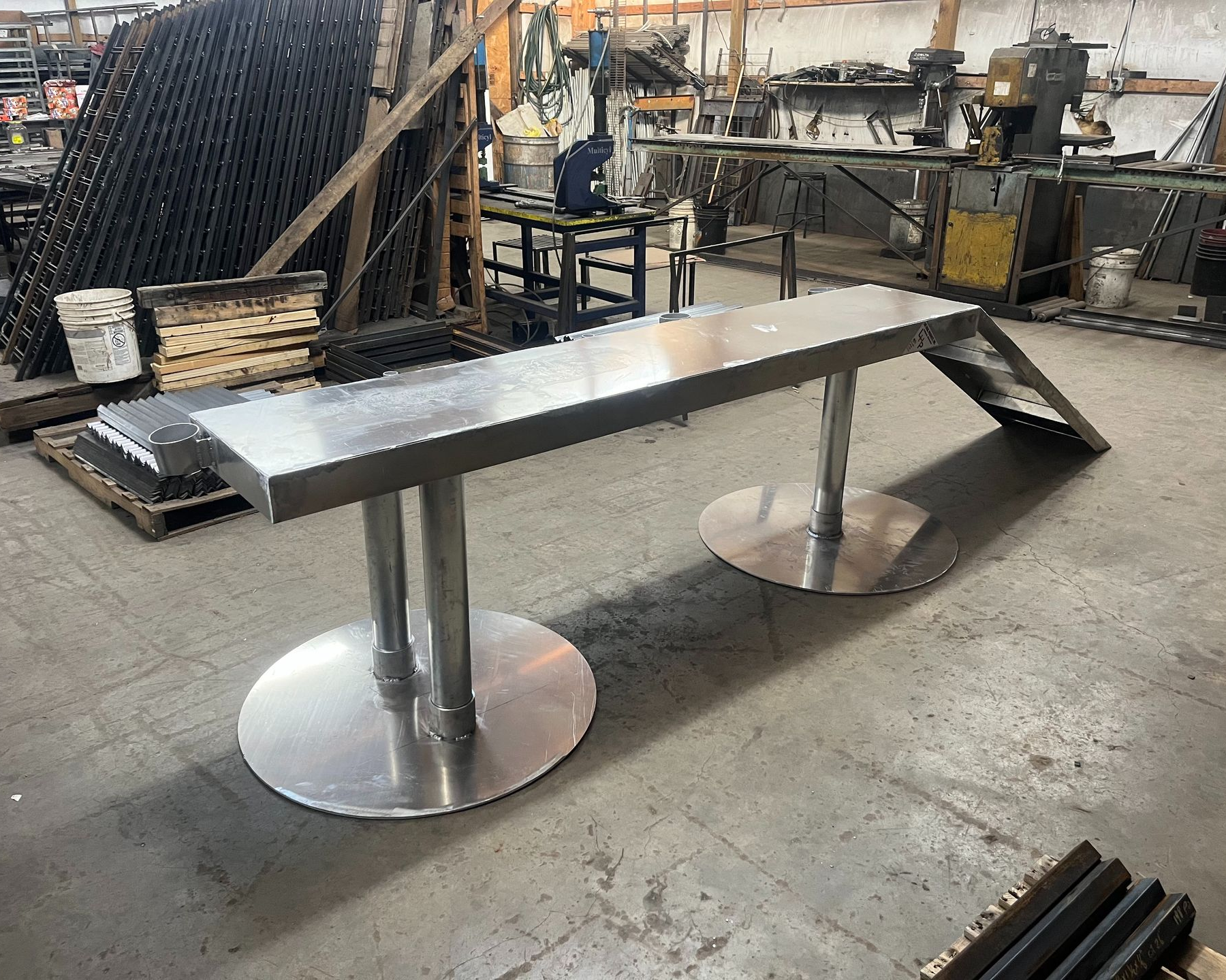 Stainless steel workbench with two round base supports in a workshop.