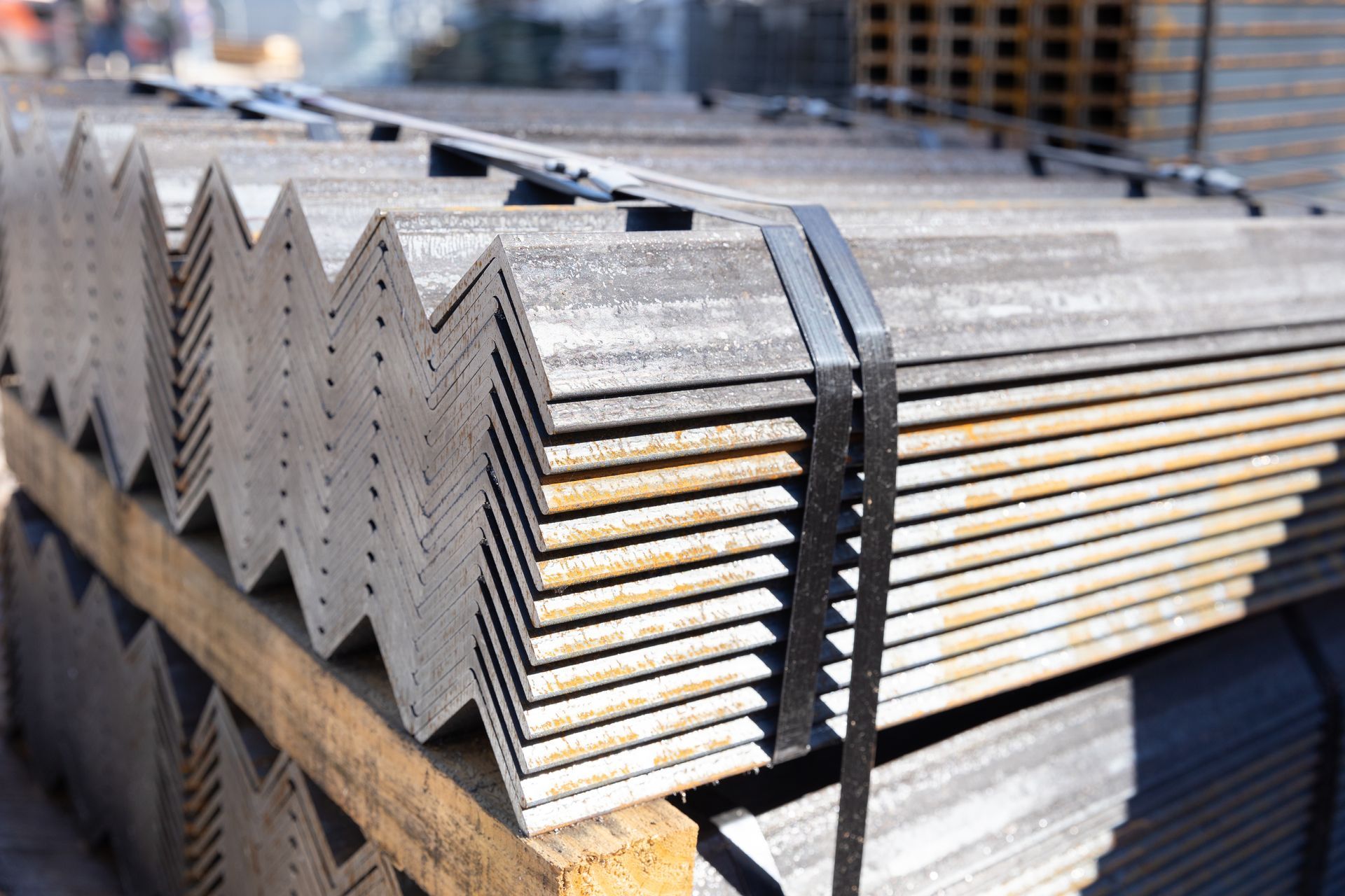 Stack of metal angle beams bound with black straps, on a wooden pallet.