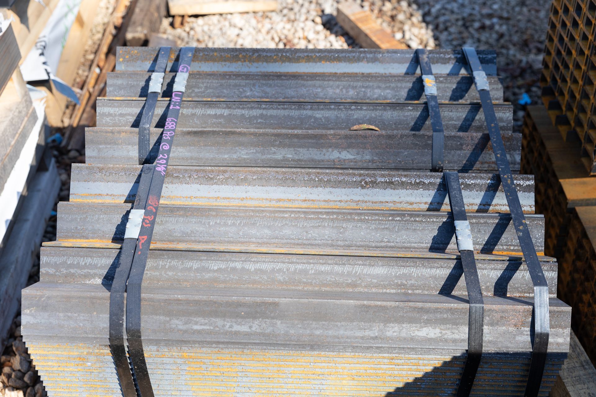 Stack of metal angle beams bound with black straps, on a wooden pallet.