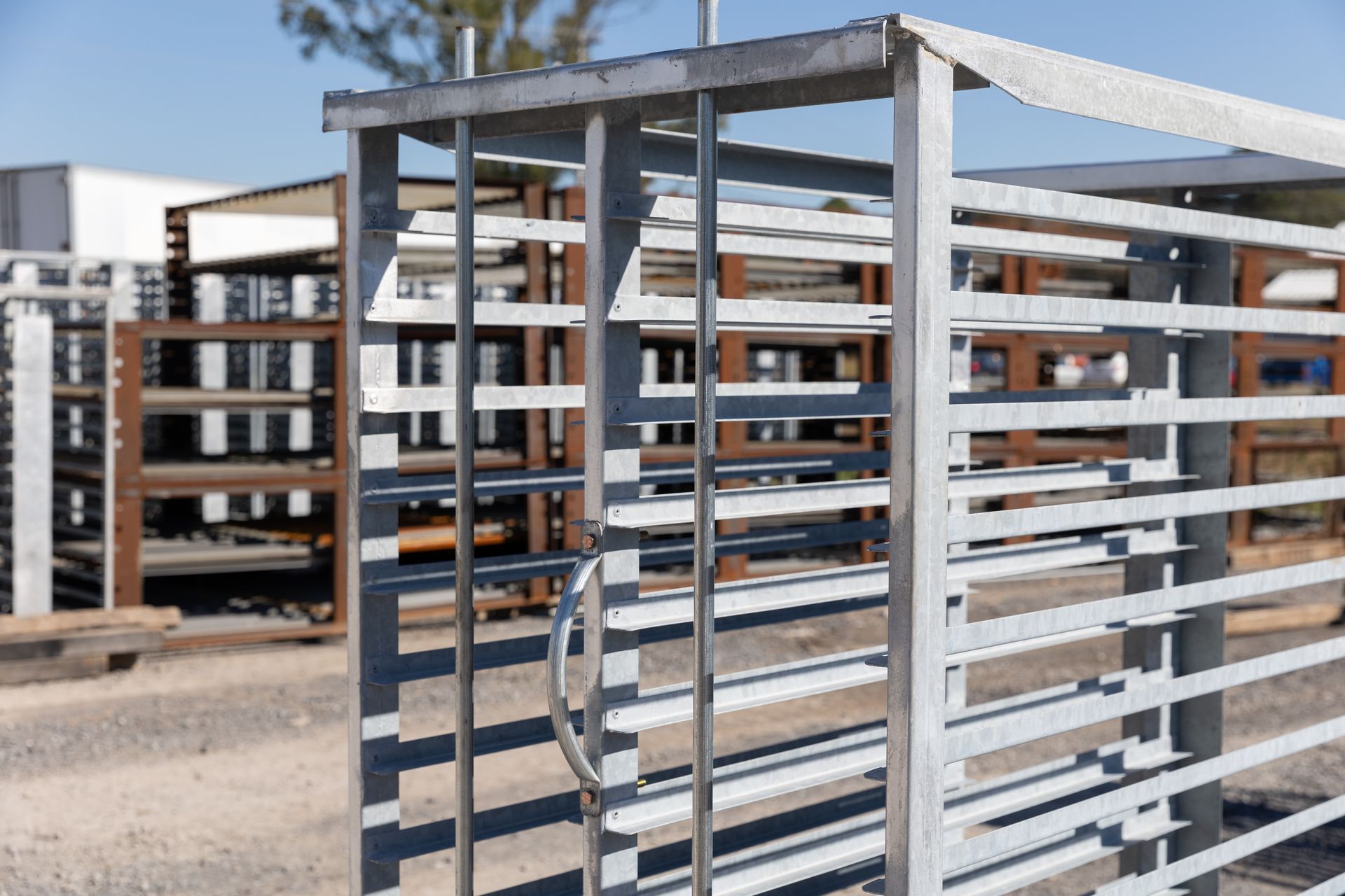 Metal storage racks outdoors. Open metal gate with a handle, other racks in background.