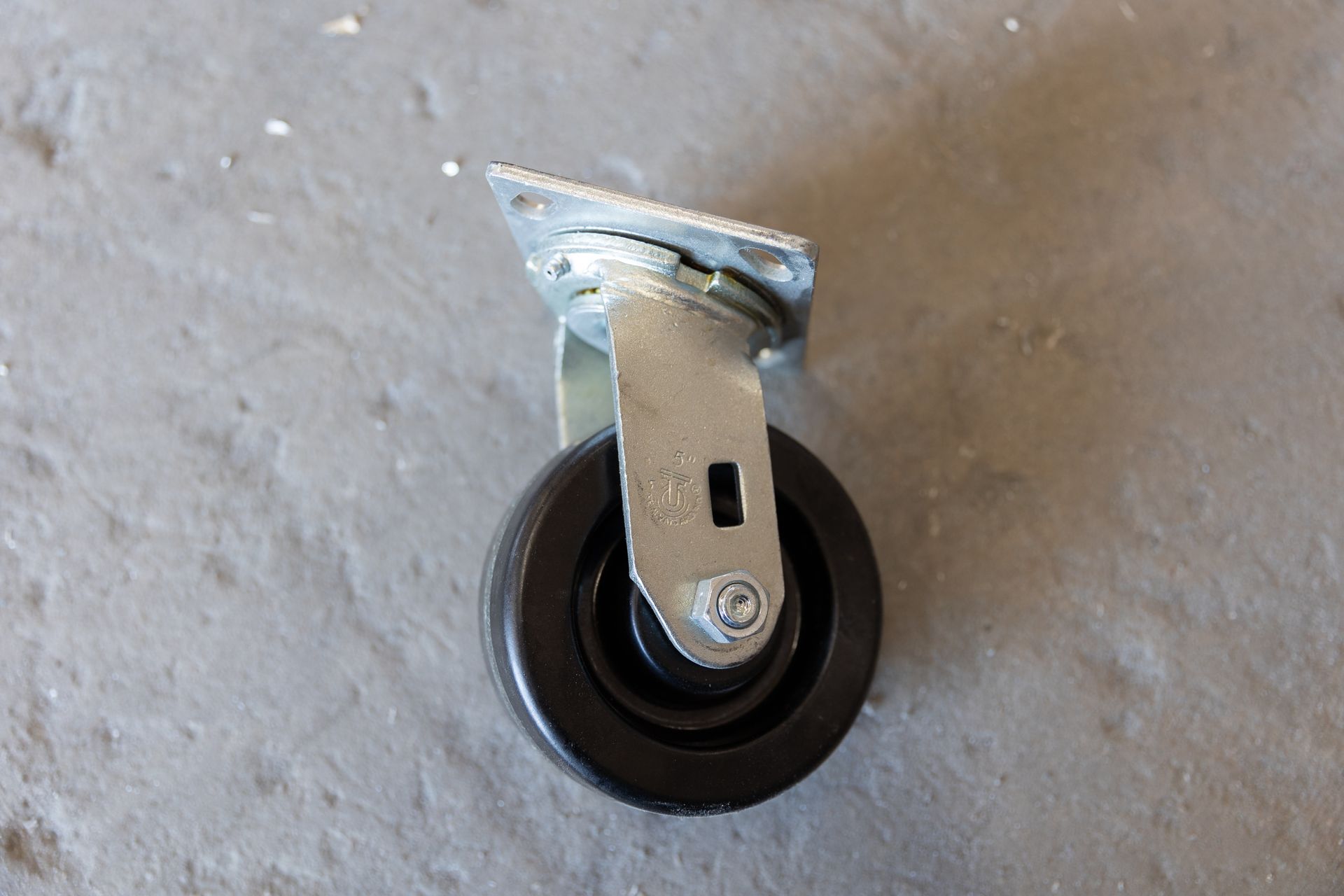 Black swivel caster wheel with mounting plate on gray surface.
