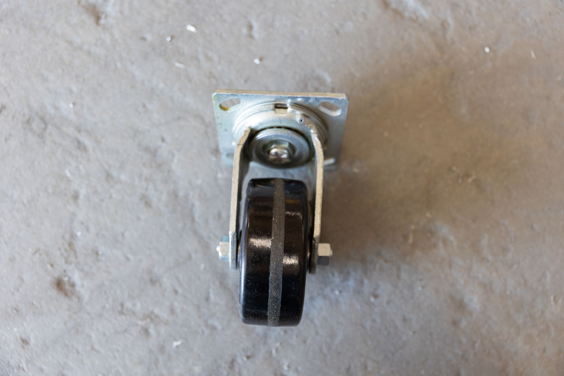 Black swivel caster wheel with mounting plate on gray surface.