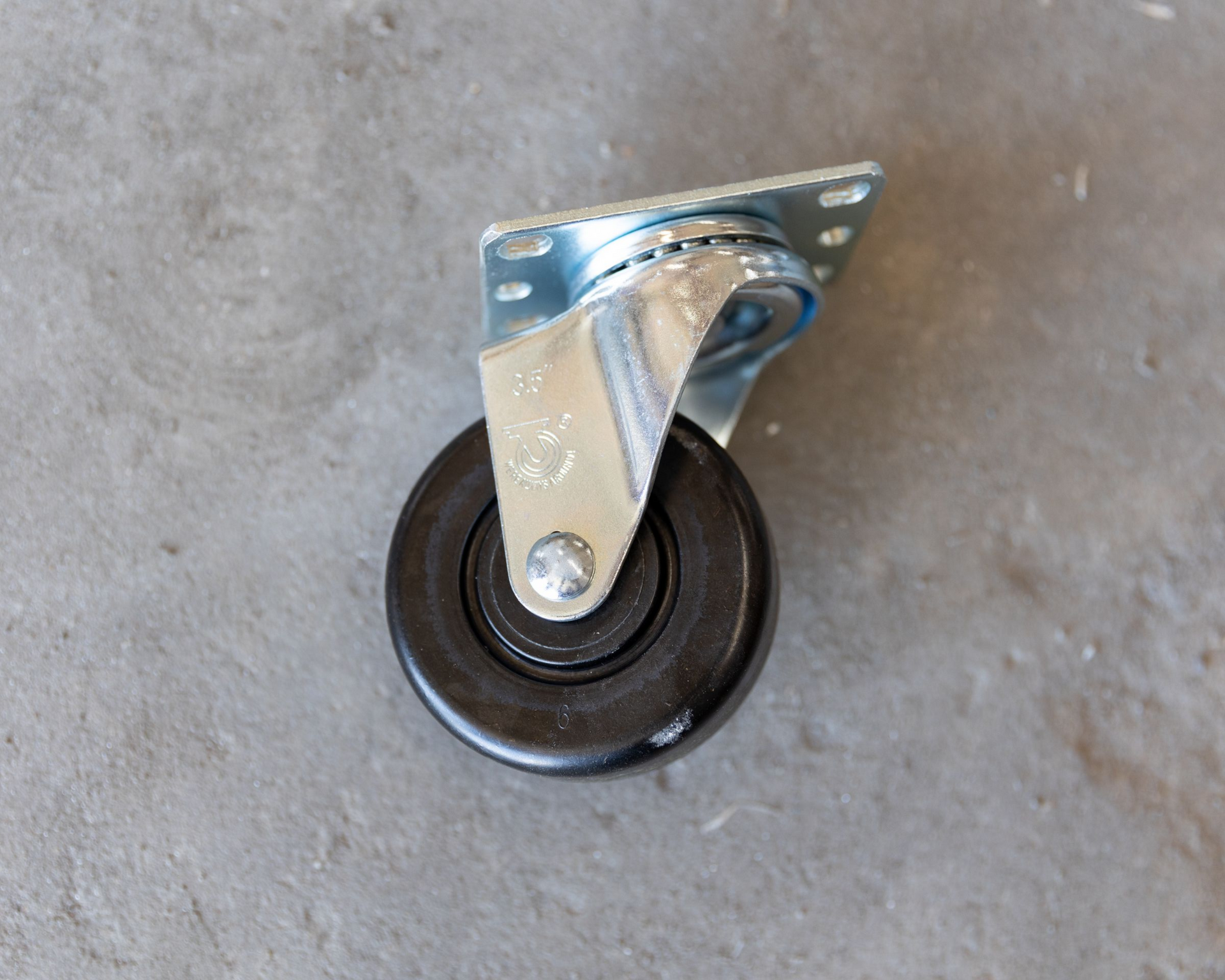 Black swivel caster wheel with mounting plate, on a gray surface.