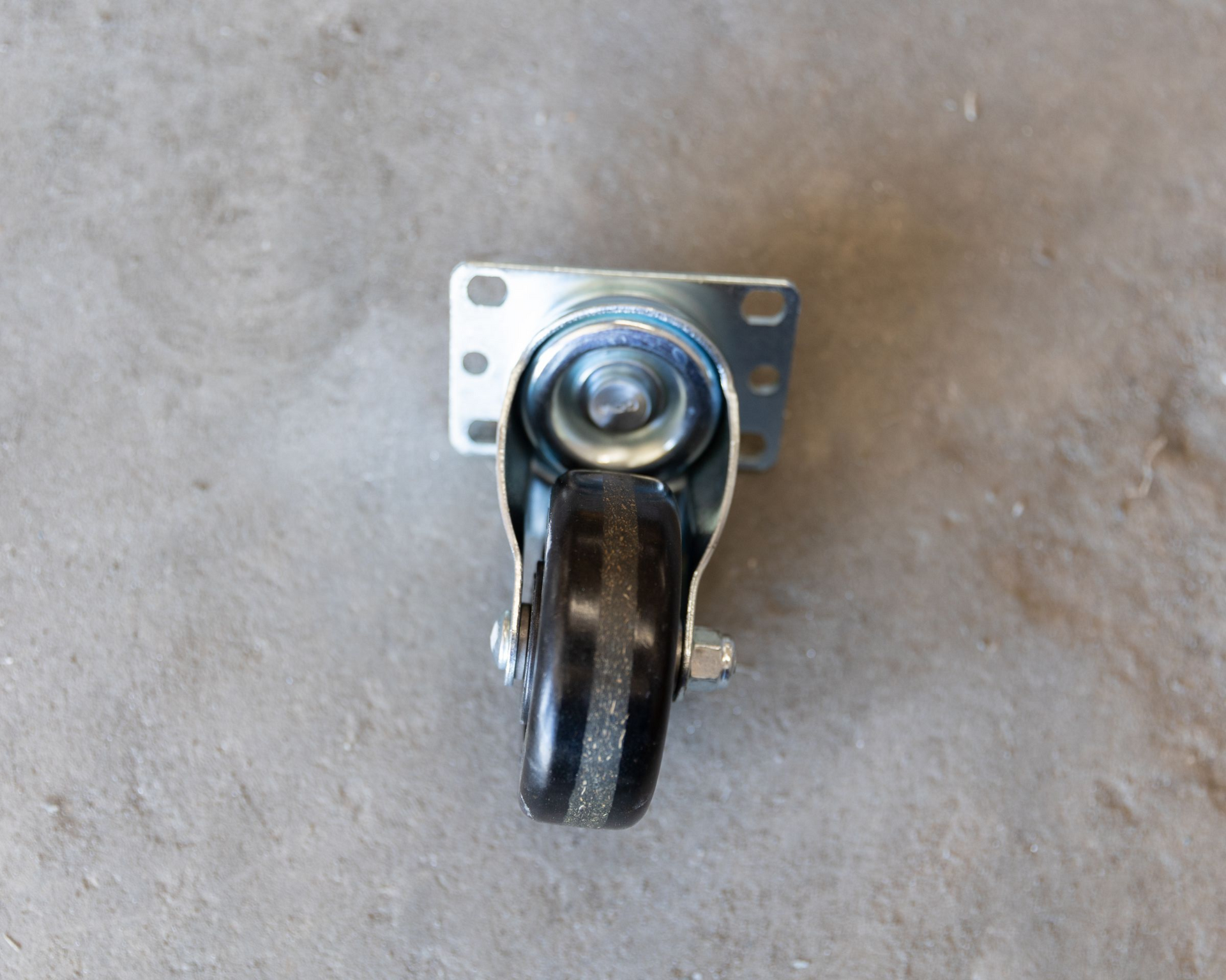 Black swivel caster wheel with mounting plate, on a gray surface.