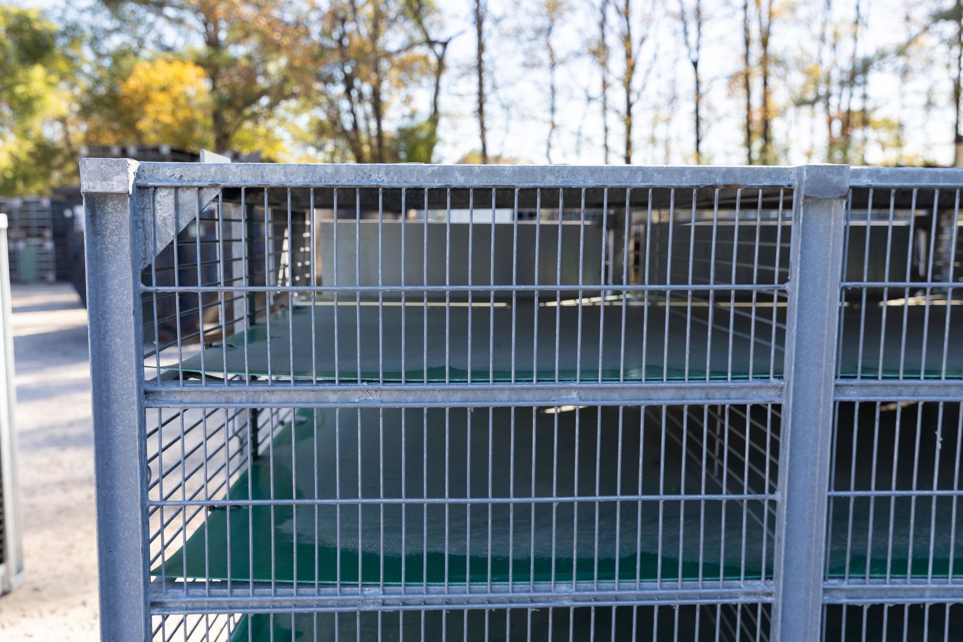 Metal storage cage with vertical bars, filled with items. Outdoor setting with trees in the background.