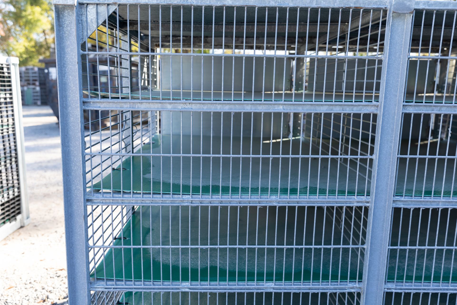 Metal storage cage with vertical bars, filled with items. Outdoor setting with trees in the background.